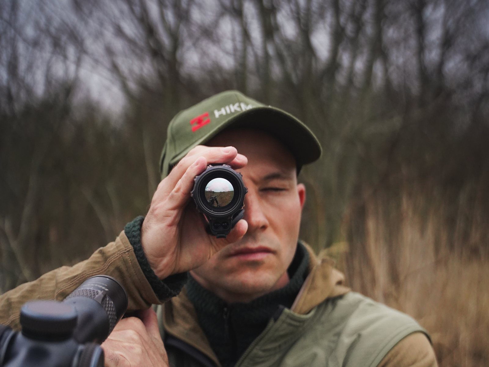 Jägare bakom geväret på åtelpasset håller HIKMICRO LYNX 3.0 termisk monokulär mot ögat